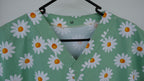 Green scrub top with white daisy pattern on a hanger against a white background