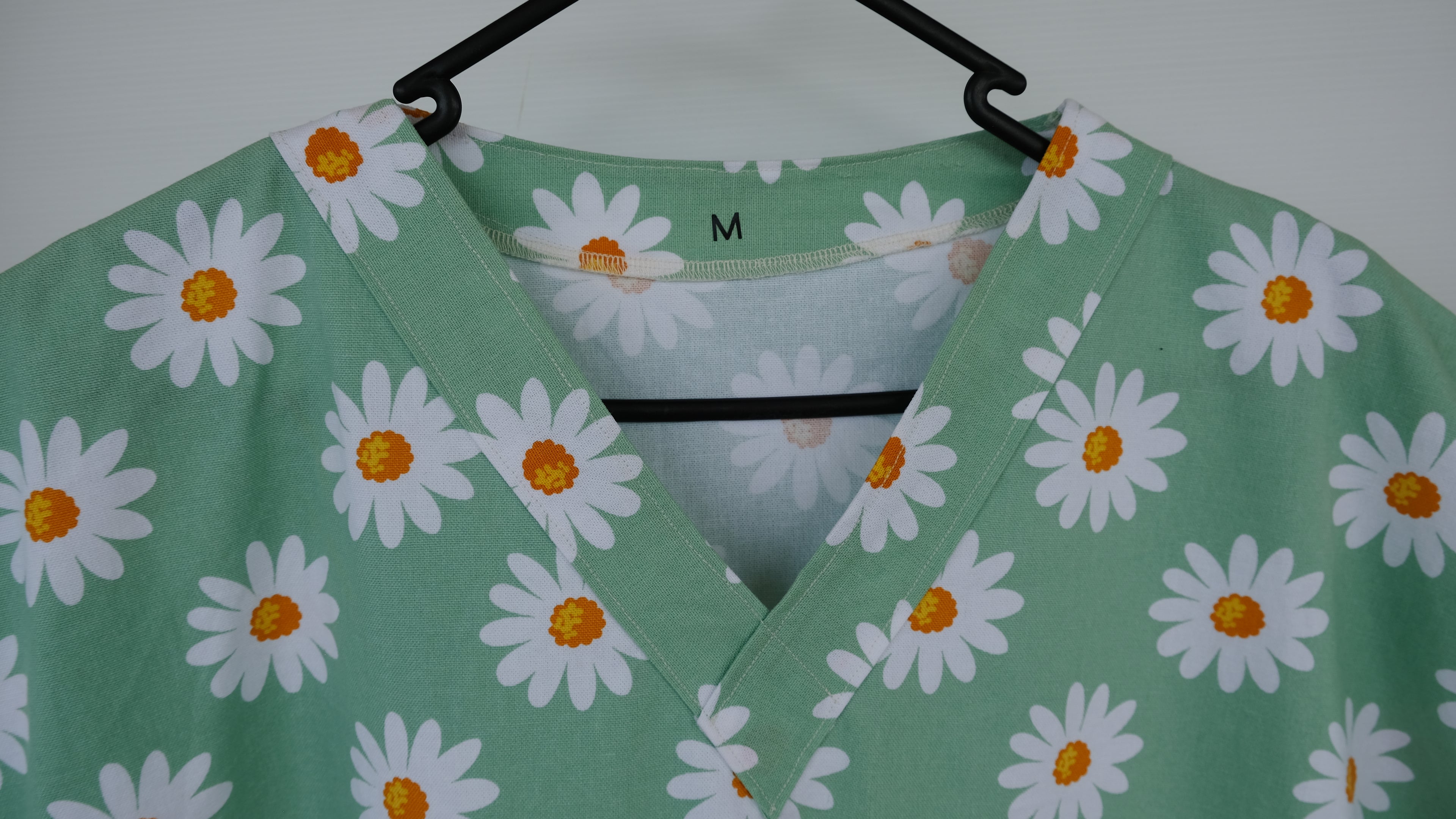 Green scrub top with white daisy pattern on a hanger against a white background