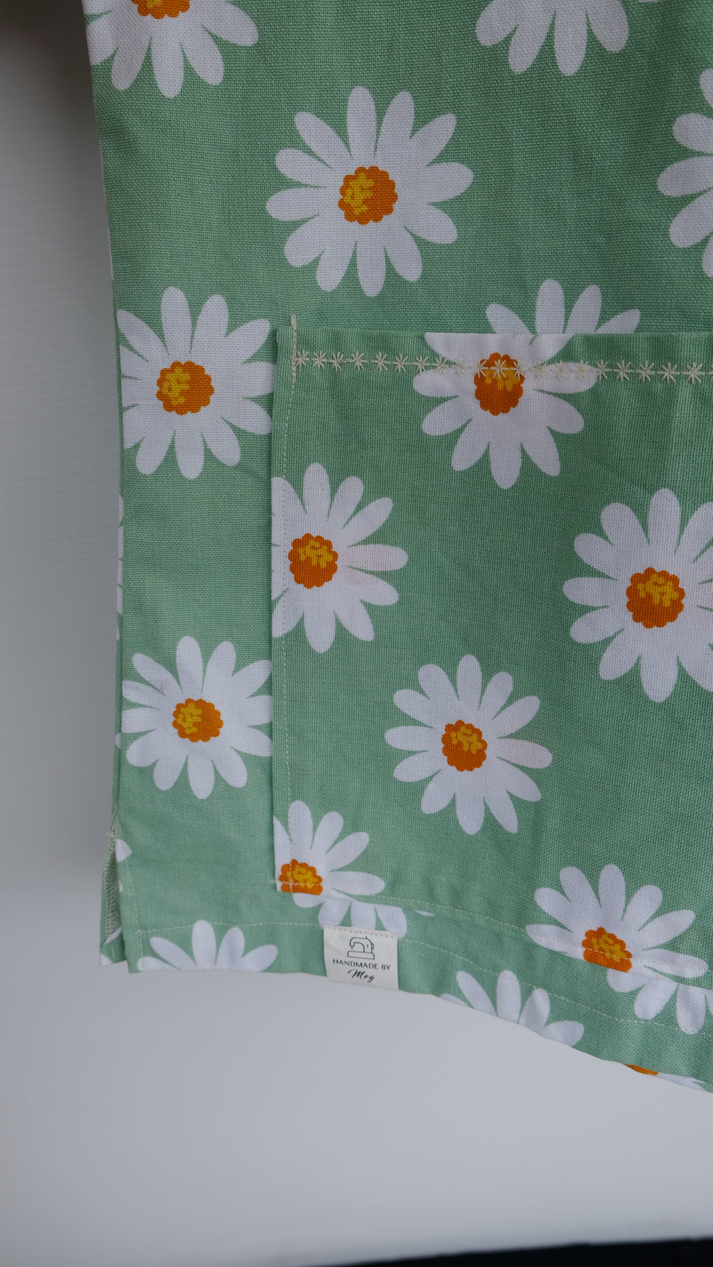 Green scrub top with white daisy pattern on a hanger against a white background