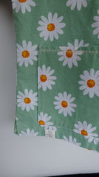 Green scrub top with white daisy pattern on a hanger against a white background