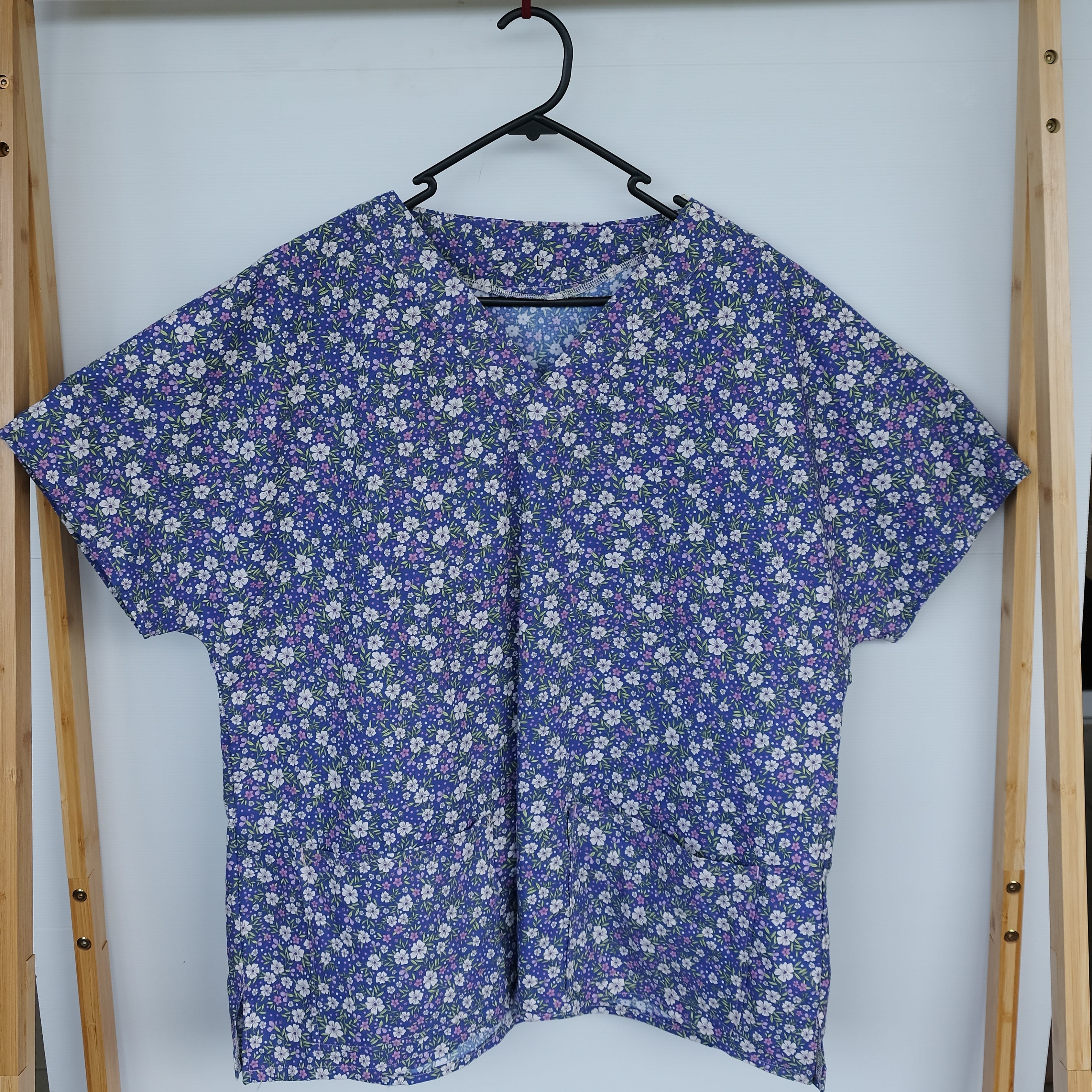 Blue floral scrub top in a wooden frame on a white background