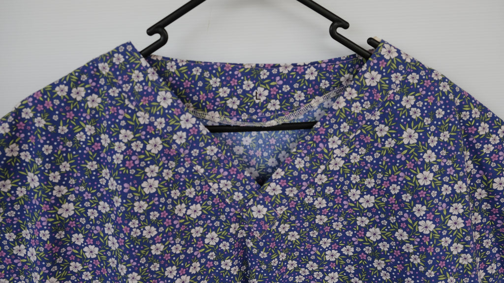 Blue and purple floral scrub top in a wooden frame on a white background

