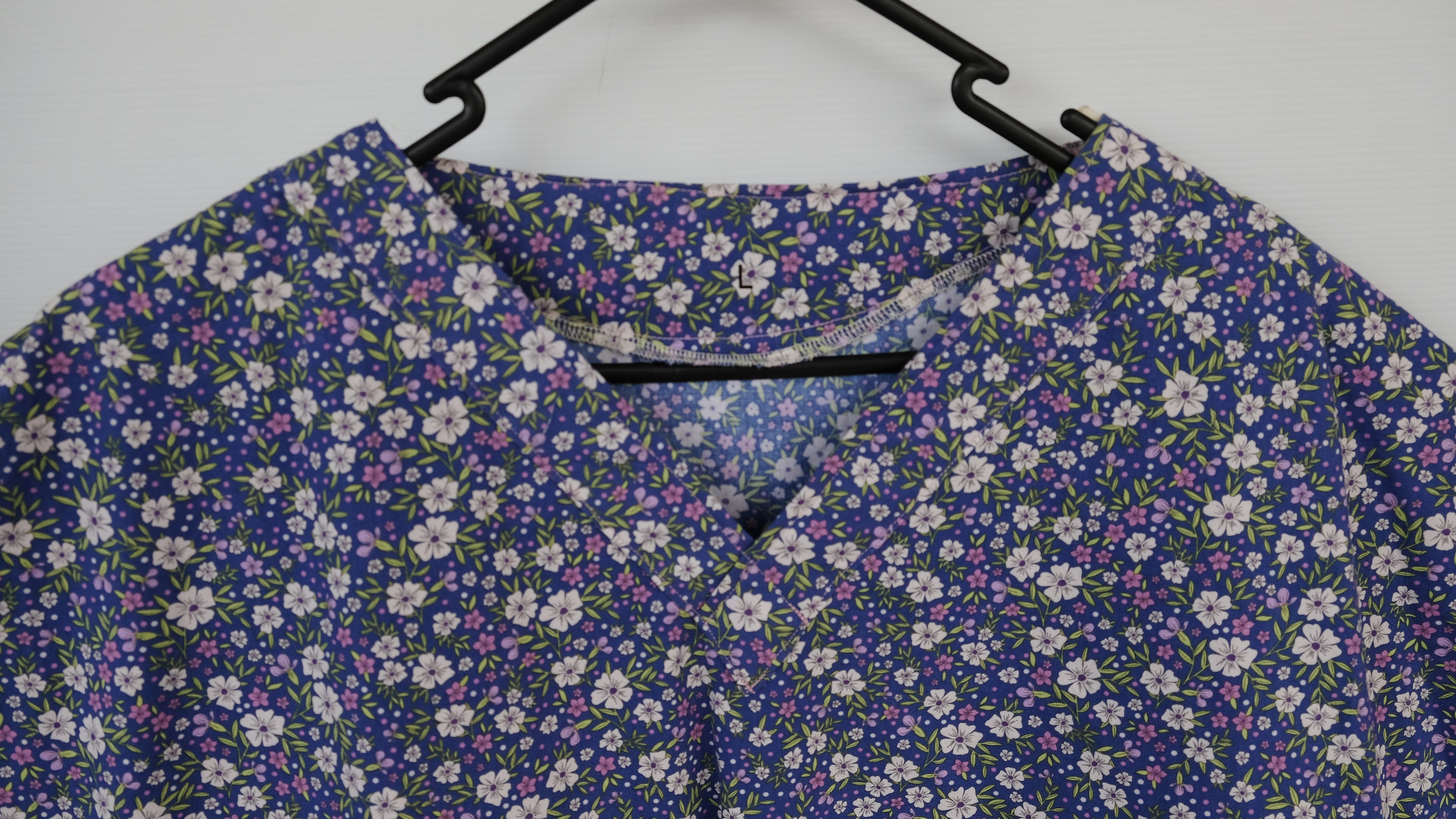 Blue and purple floral scrub top in a wooden frame on a white background
